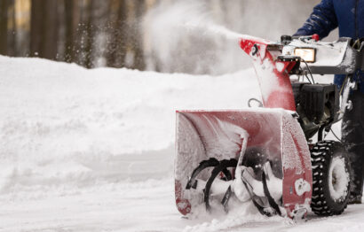A man with a red snow-covered snow blower clears the area from snow. Clearing the area from snowfall.