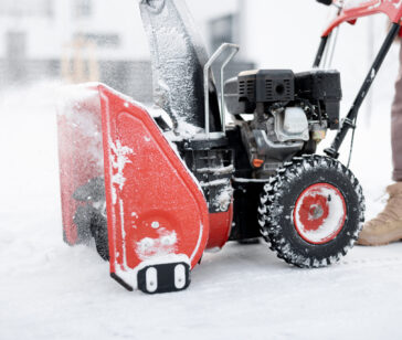 Person pushing a snow thrower machine, cleaning a pathway from the snow, close-up on machine that blows snow away
