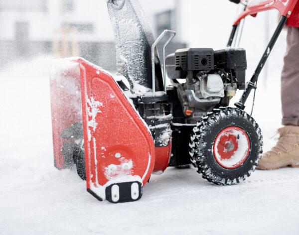 Person pushing a snow thrower machine, cleaning a pathway from the snow, close-up on machine that blows snow away